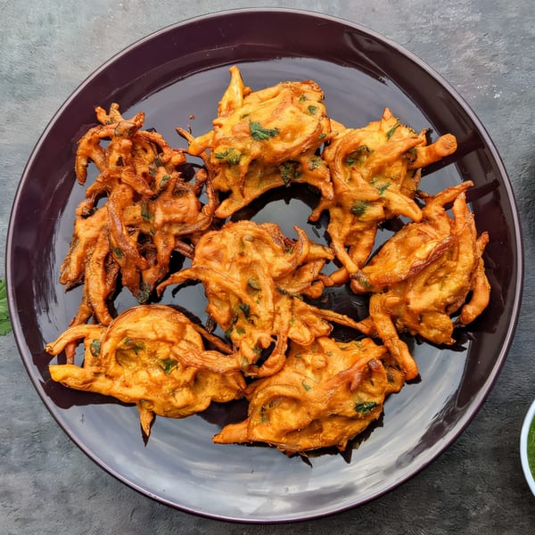 A dark plate filled with golden-brown, crispy Indian onion bhaji, garnished with green herbs.