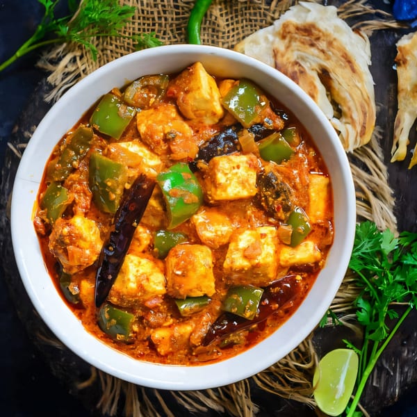 A white bowl of Indian paneer curry with green bell peppers, dried chilies, and cilantro.